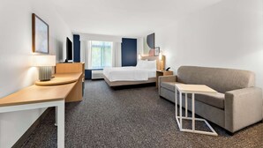 Una habitación de hotel con cama, sofá, escritorio y lámpara.