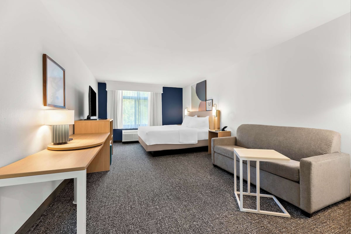 A hotel room with a bed, a sofa, a desk, and a lamp.