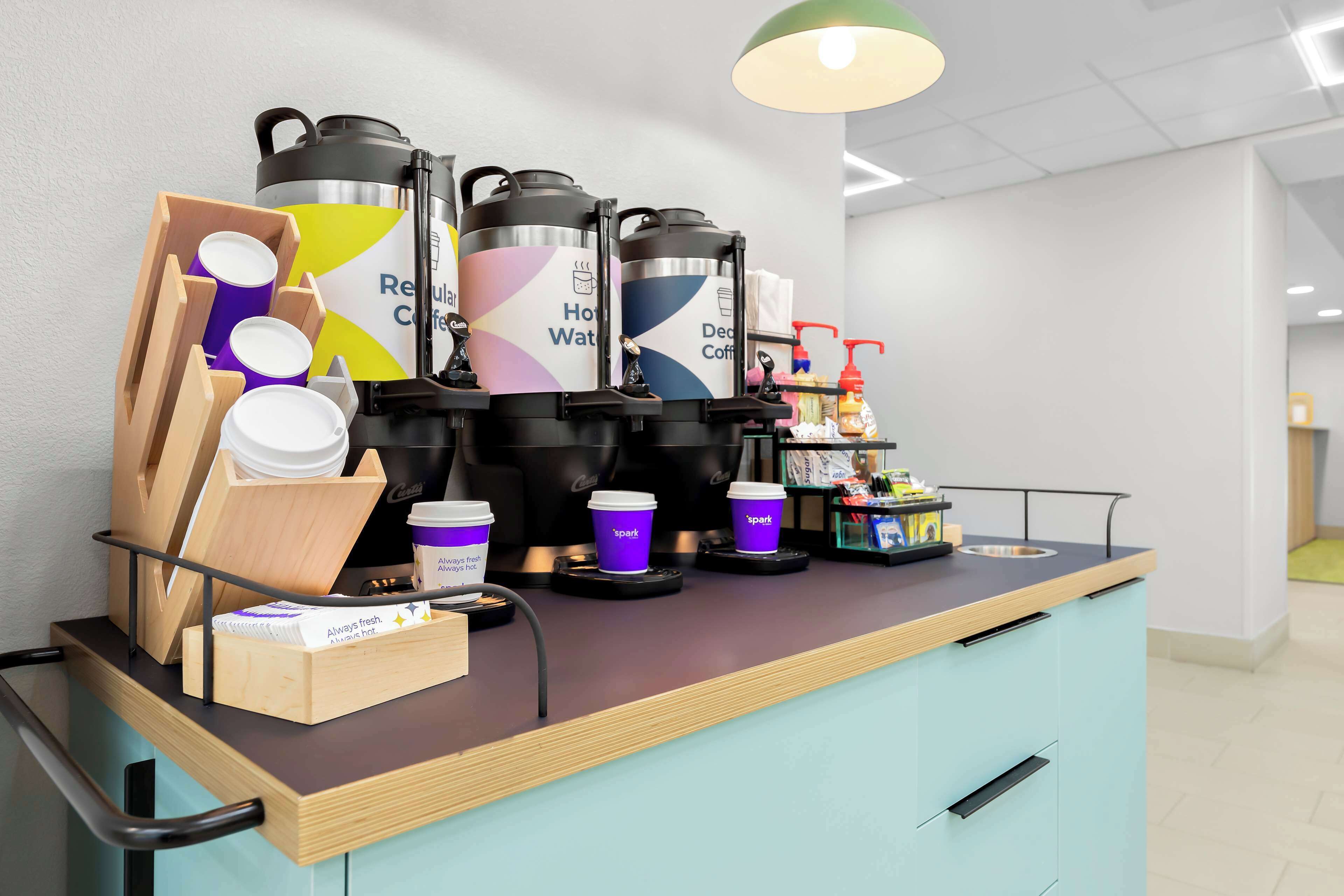 A coffee station with multiple coffee dispensers, disposable cups, and a coffee machine.