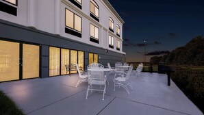 Un edificio moderno con amplios ventanales y un patio amoblado con mobiliario metálico blanco.