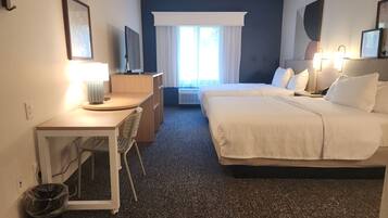 Una habitación de hotel con escritorio, dos camas, una silla, un cesto de basura y una ventana con cortinas.