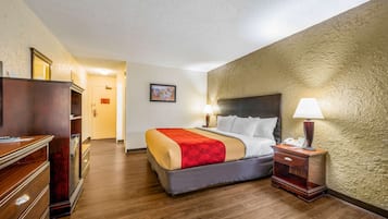 Una habitación de hotel con una cama, mesitas de noche, un aparador y una puerta que da a otra habitación.