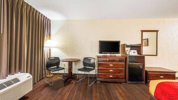 Habitación de hotel con cama, televisión, cómoda, escritorio, dos sillas, lámpara y calefactor.