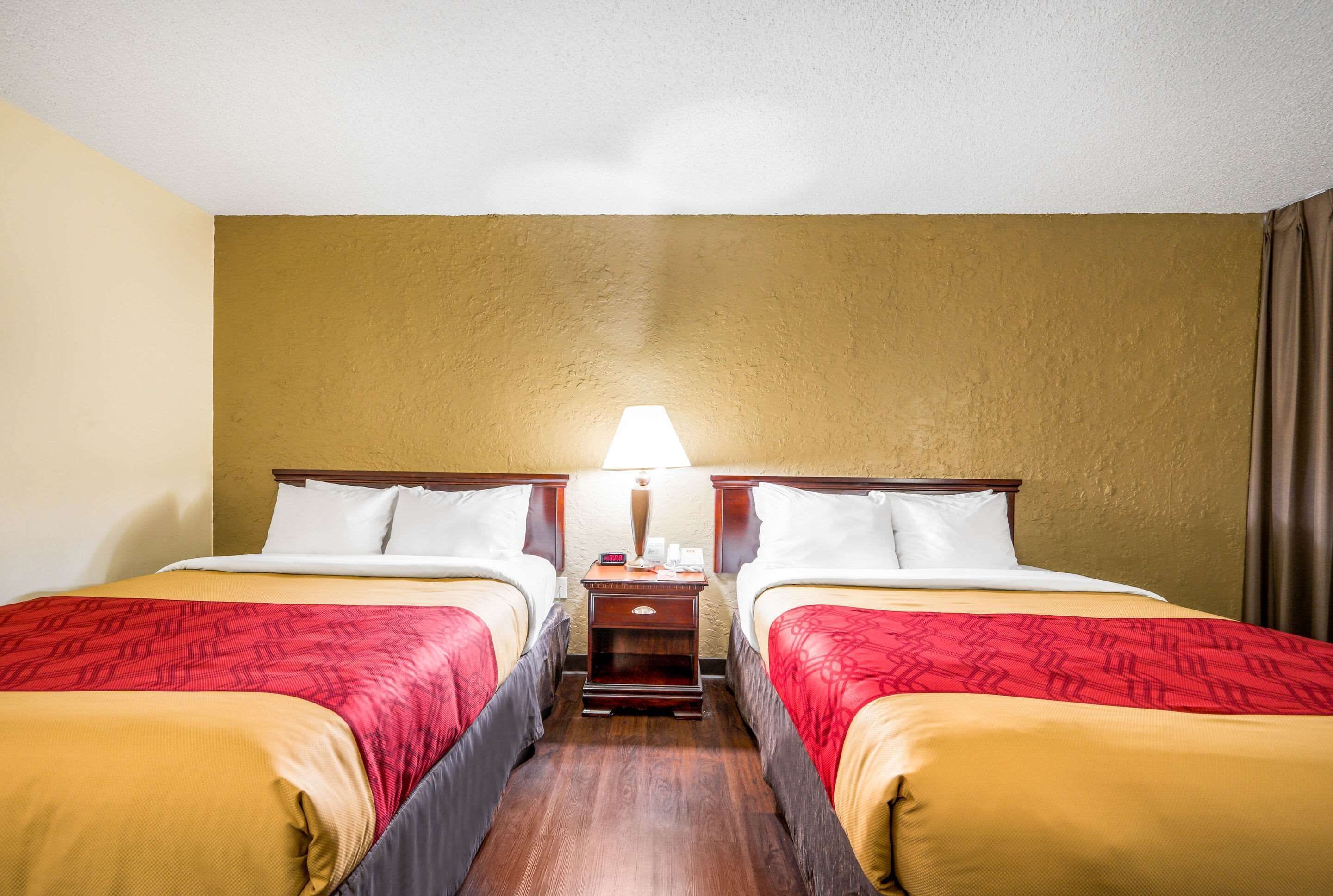 Quarto de hotel com duas camas, uma mesinha de cabeceira e uma luminária.
