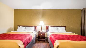 Quarto de hotel com duas camas, uma mesinha de cabeceira e uma luminária.