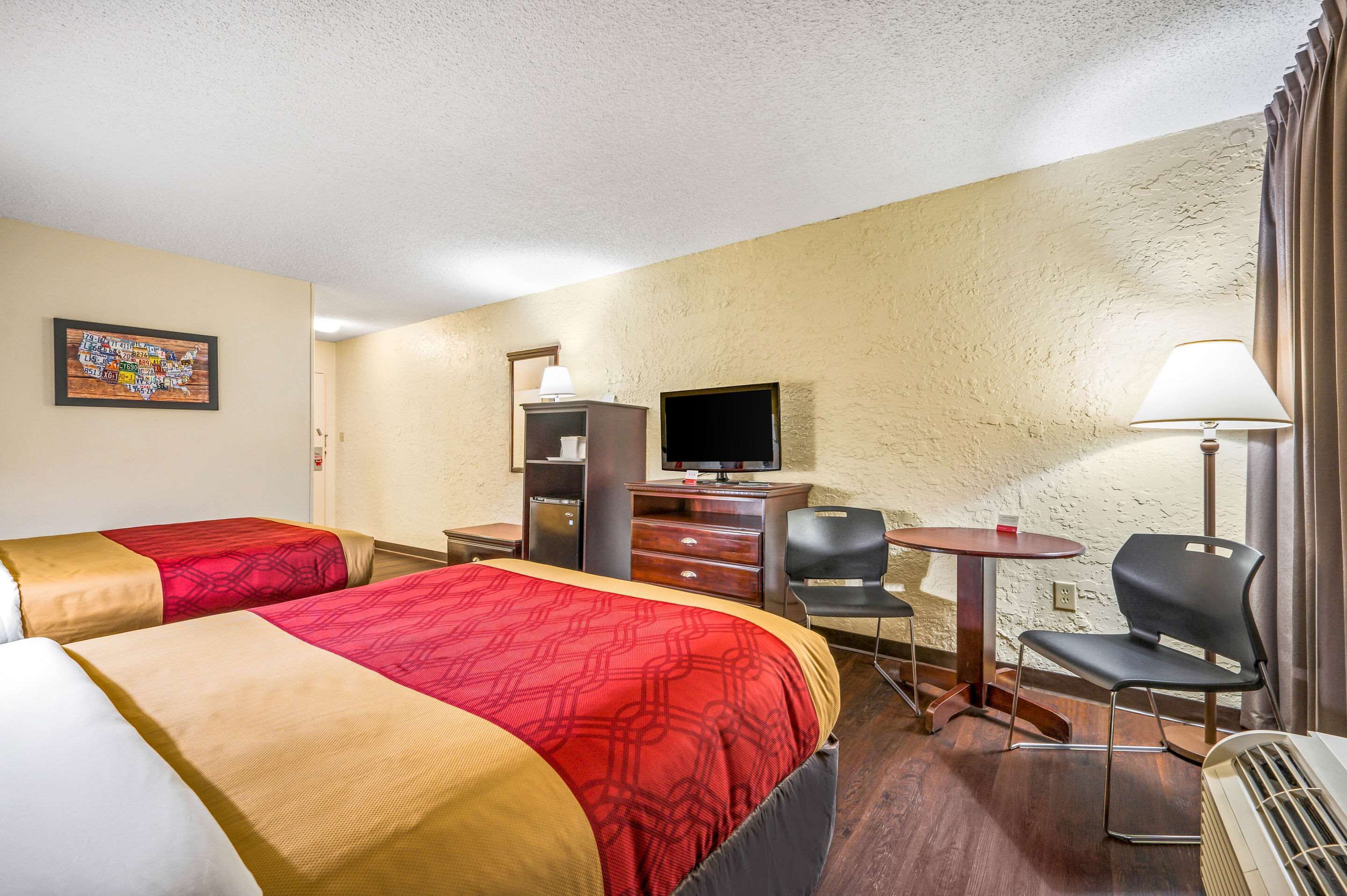 Habitación de hotel con dos camas, un escritorio con televisor, una silla y una mesa.