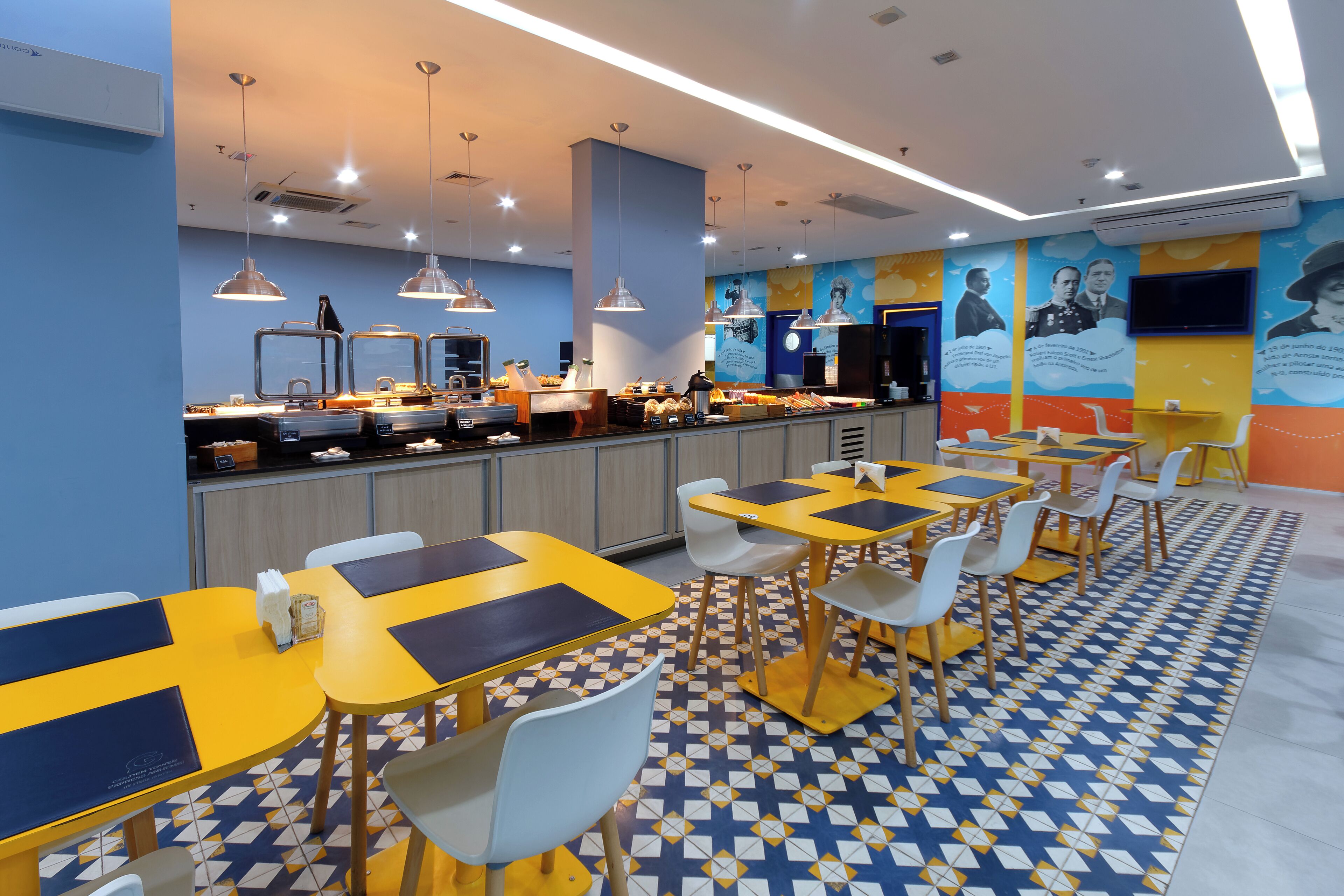 Un restaurante moderno con mesas amarillas y azules, sillas blancas y un suelo con estampado.