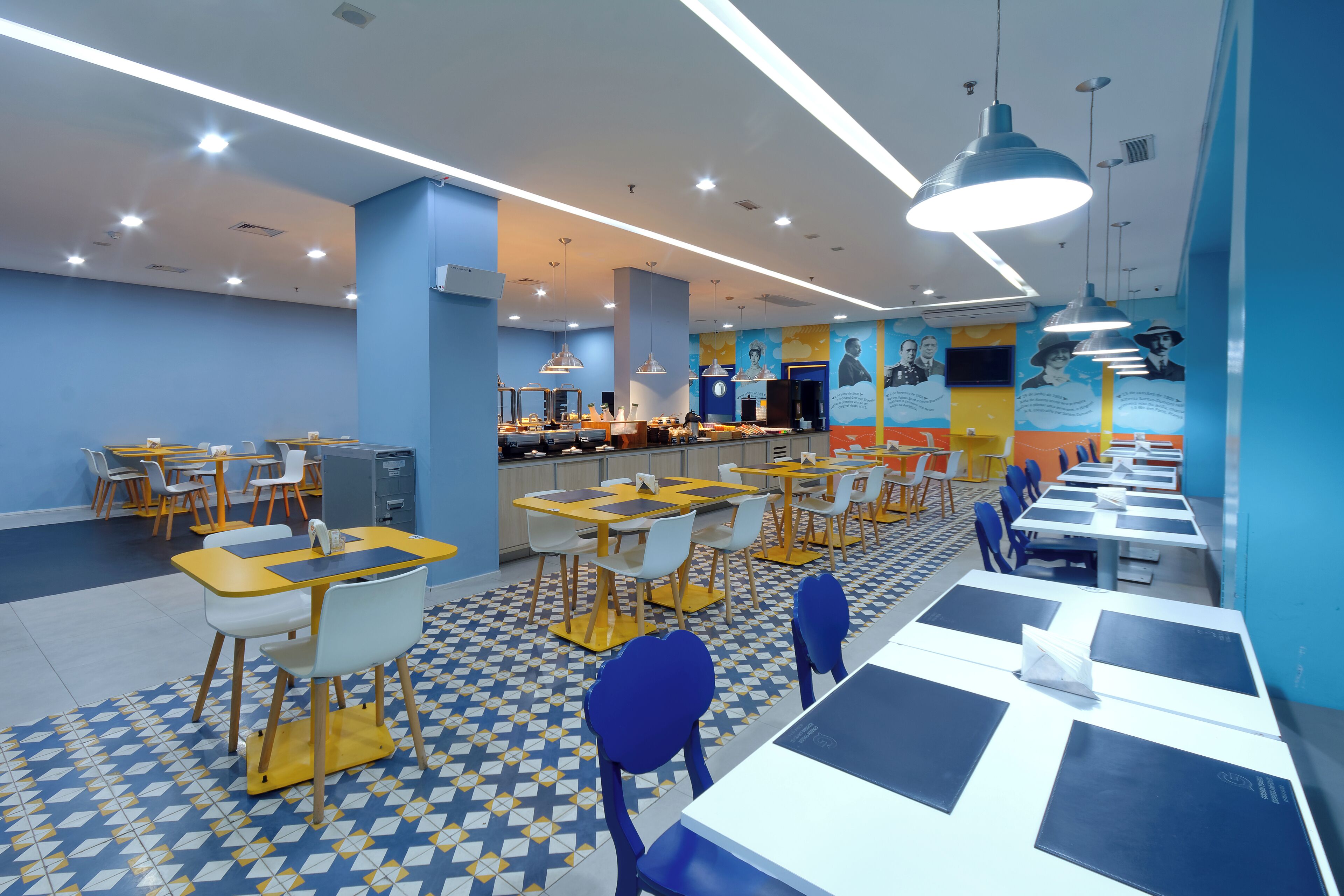 A brightly lit cafeteria with multiple tables and chairs, featuring a geometric patterned floor and blue walls.