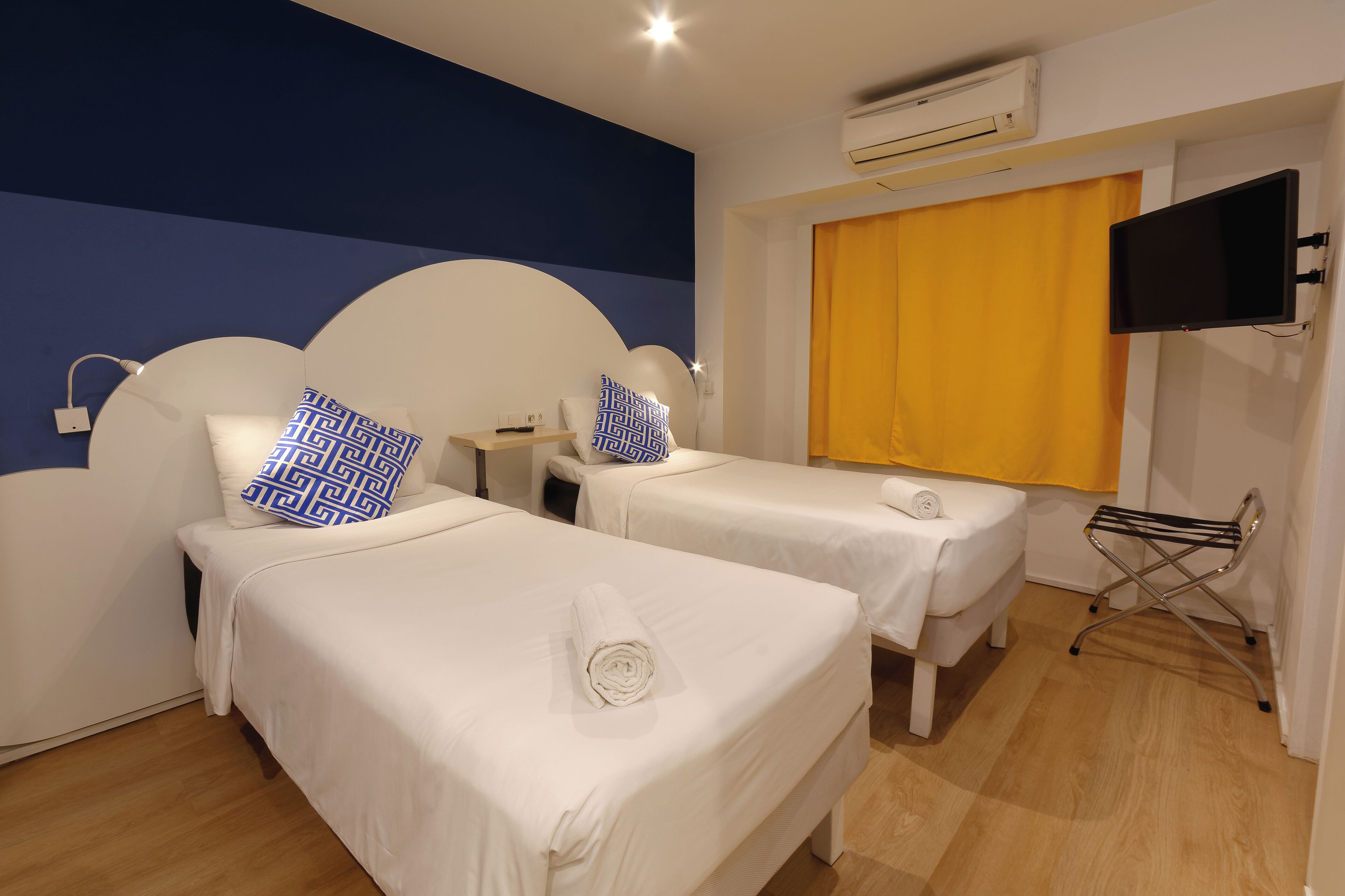 Quarto de hotel com duas camas, televisão, ar condicionado e cortina amarela.