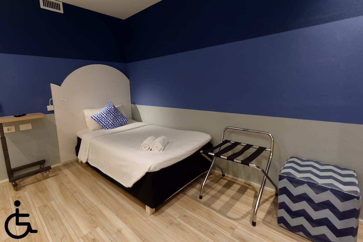 A room with a bed, a chair, a small table, and a storage ottoman.