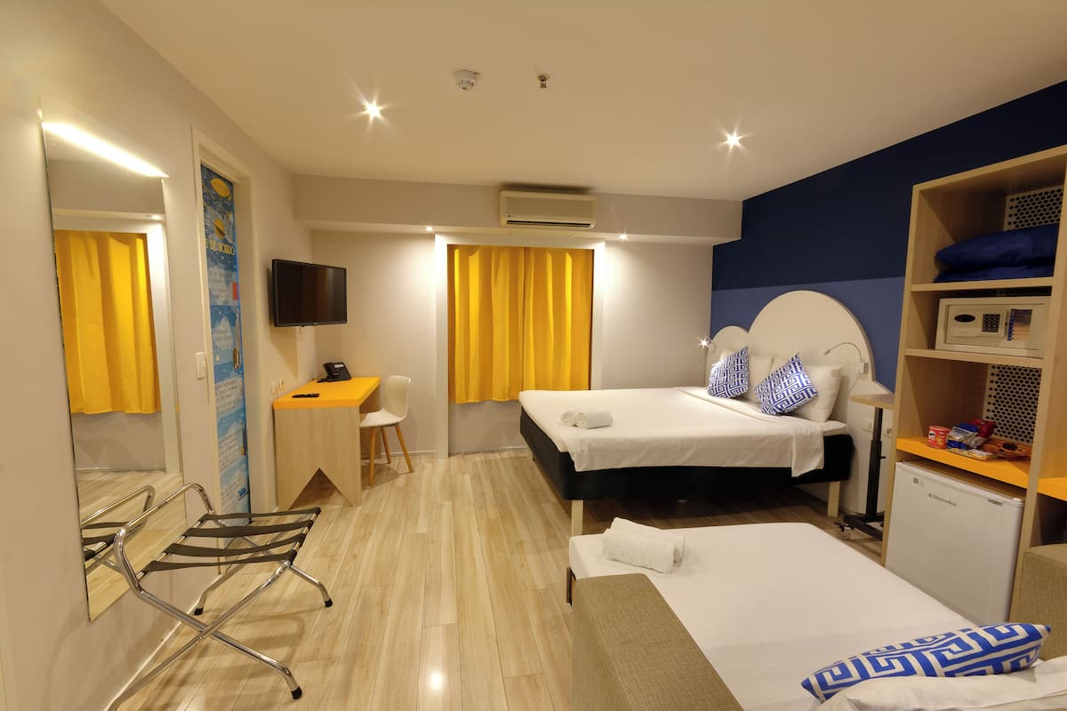 A hotel room with a bed, bedside table, desk, chair, and a small kitchenette.