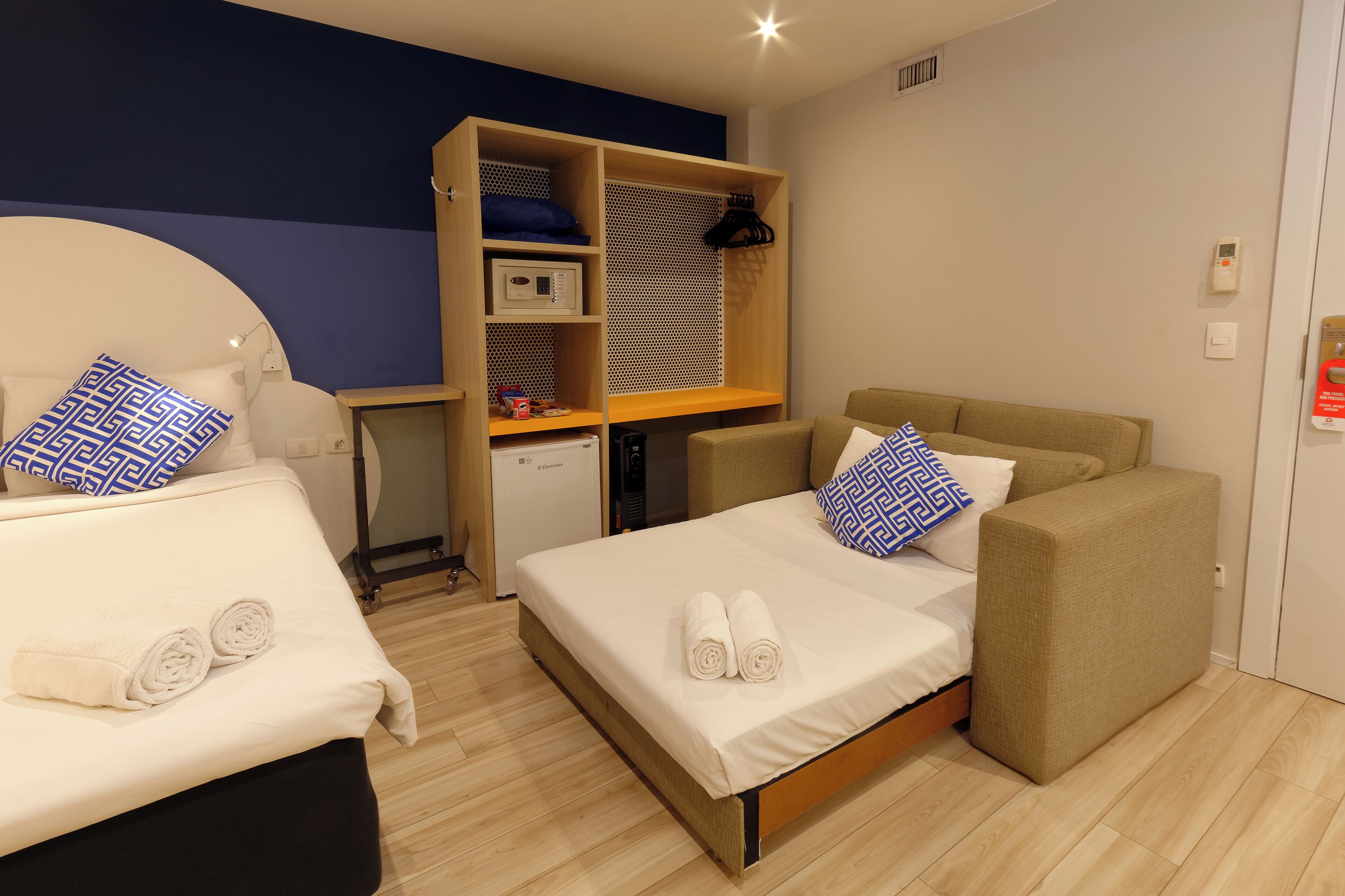 Quarto de hotel com duas camas, uma escrivaninha e um guarda-roupa.