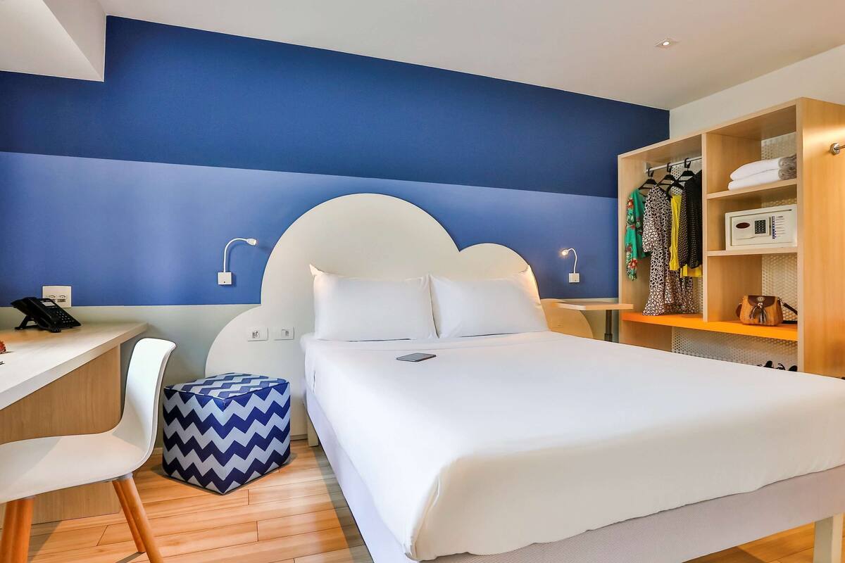 A hotel room with a bed, desk, chair, and wardrobe.