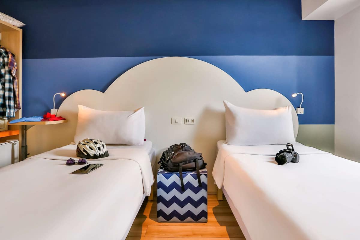 A hotel room with two beds, a wooden nightstand, a desk, and a chair.