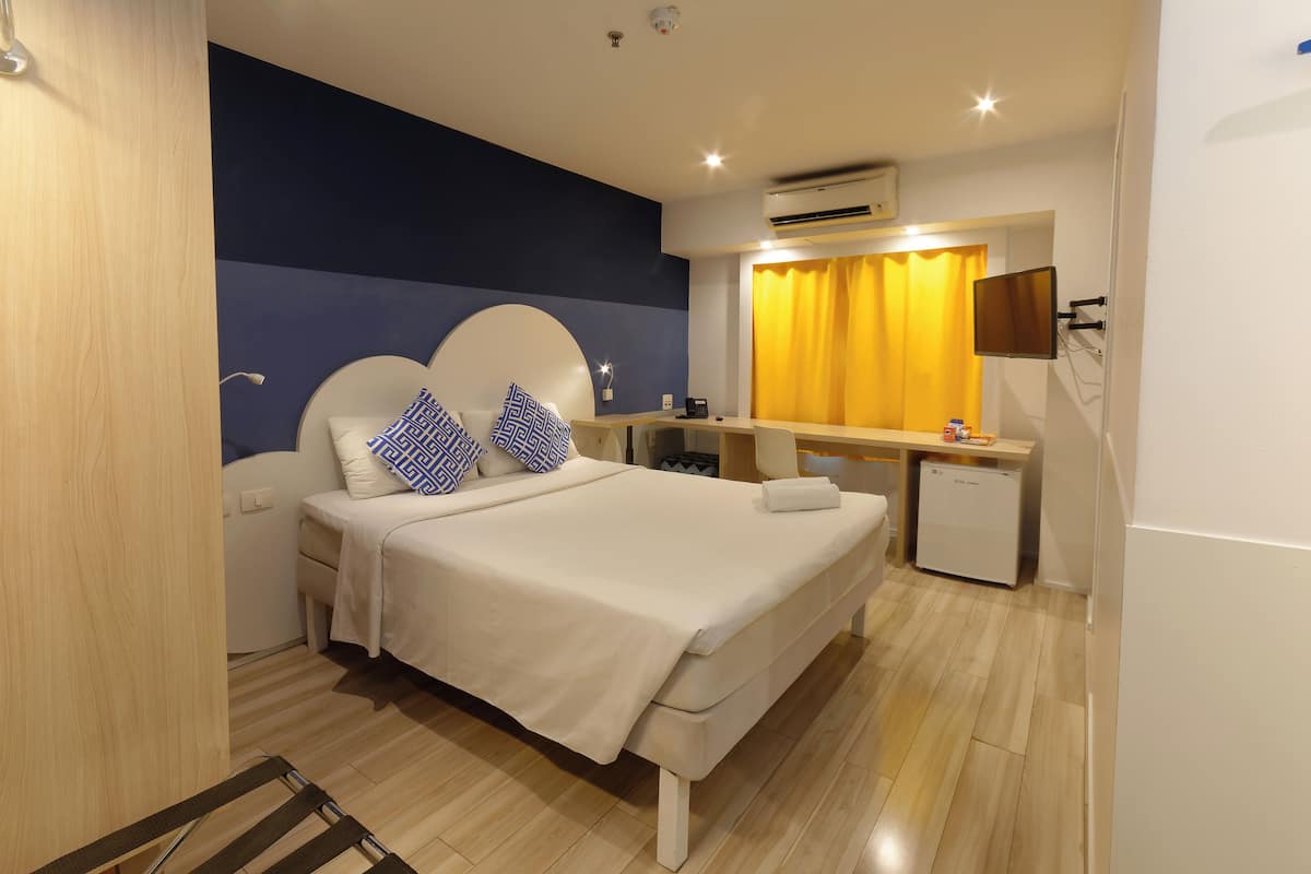 A modern hotel room with a bed, bedside table, and a small desk with a chair.