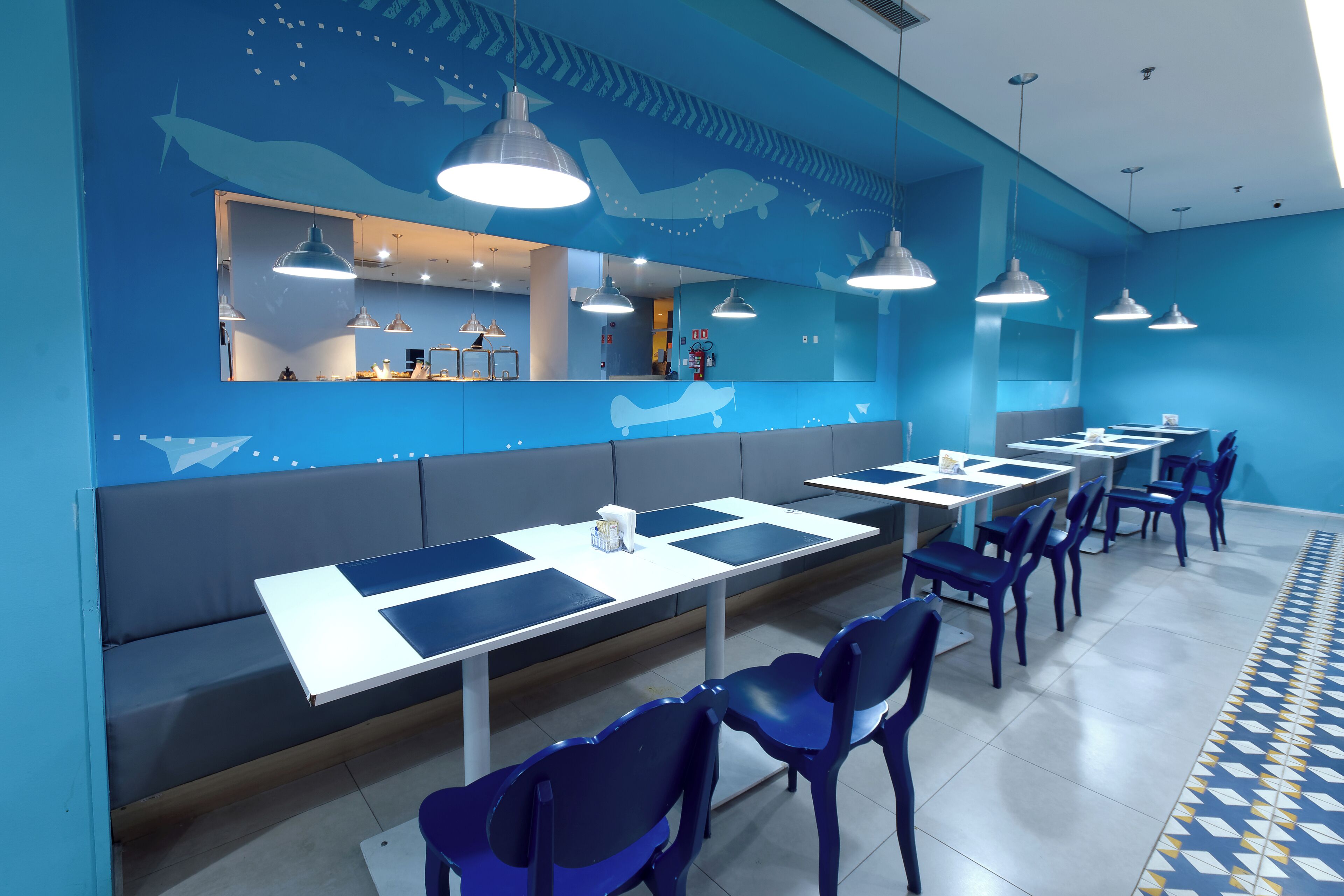 Un restaurante moderno con decoración azulada, que incluye una larga barra con mesas y sillas, y una zona de estar con bancos.
