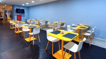 A dining area with tables and chairs, a fire extinguisher, and a television on the wall.