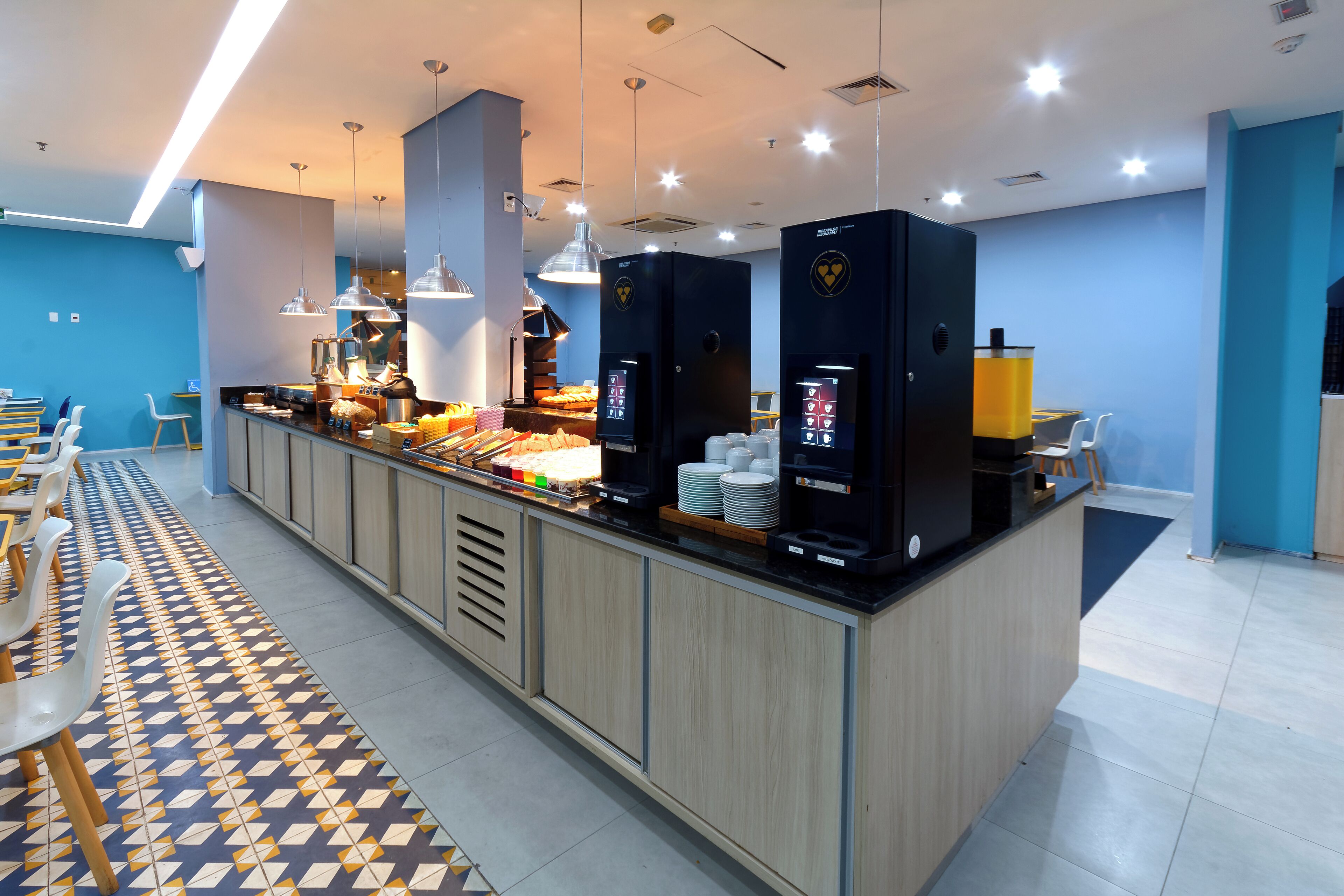 A modern breakfast bar with seating, a coffee station, and a counter with food items.