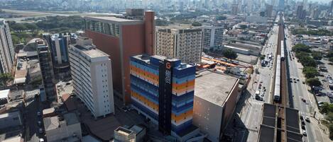 Un edificio alto con varios pisos, rodeado de otros edificios y una calle concurrida llena de vehículos.