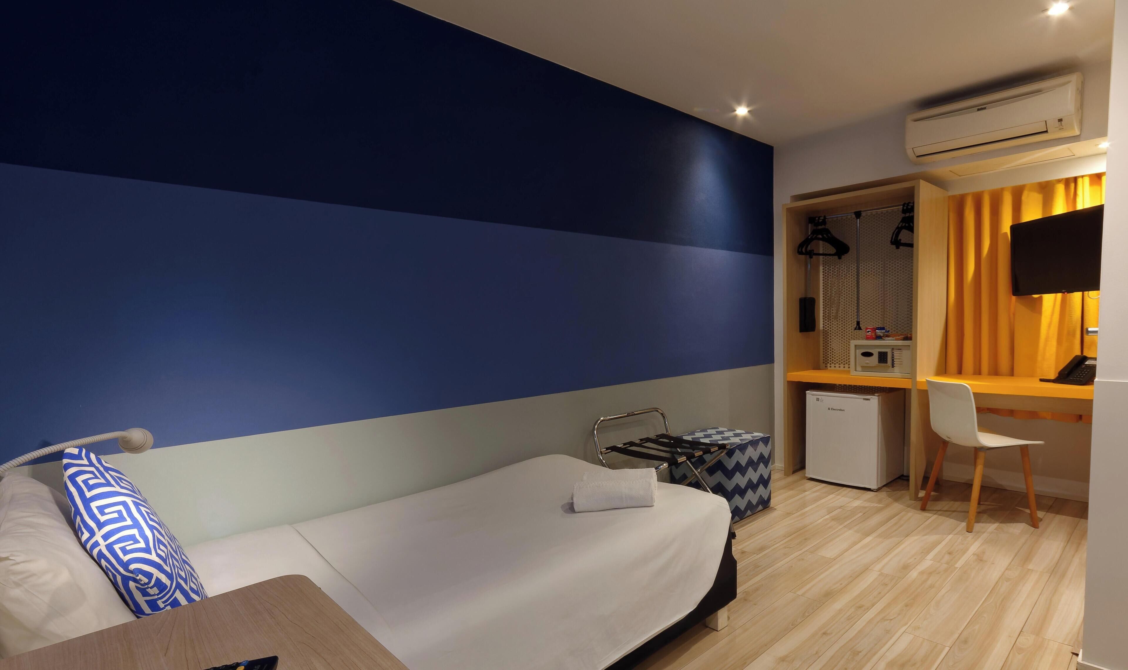 Habitación de hotel con cama, escritorio, silla, refrigerador pequeño y aire acondicionado.