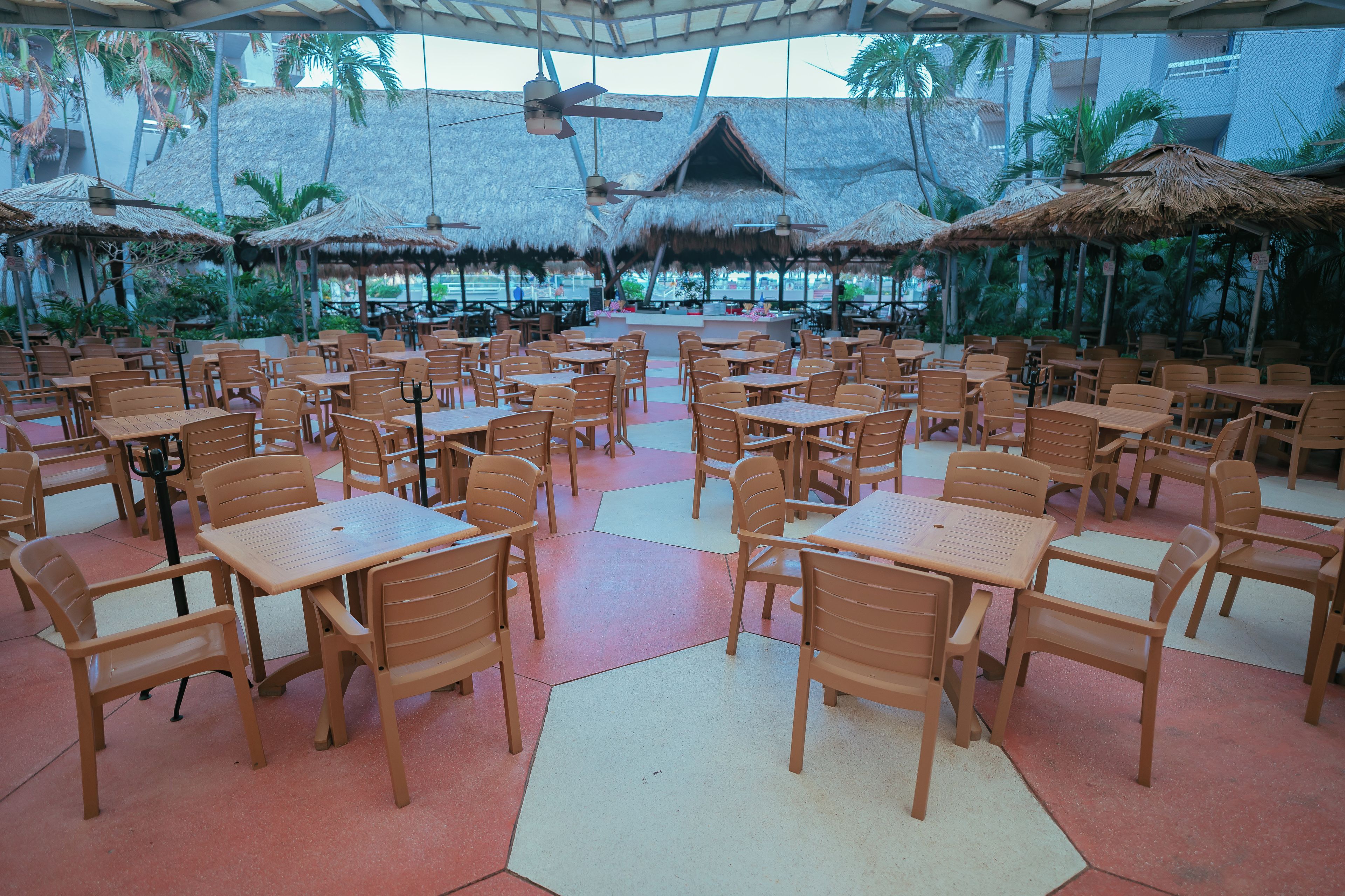 A spacious outdoor dining area with thatched umbrellas and wooden tables and chairs.