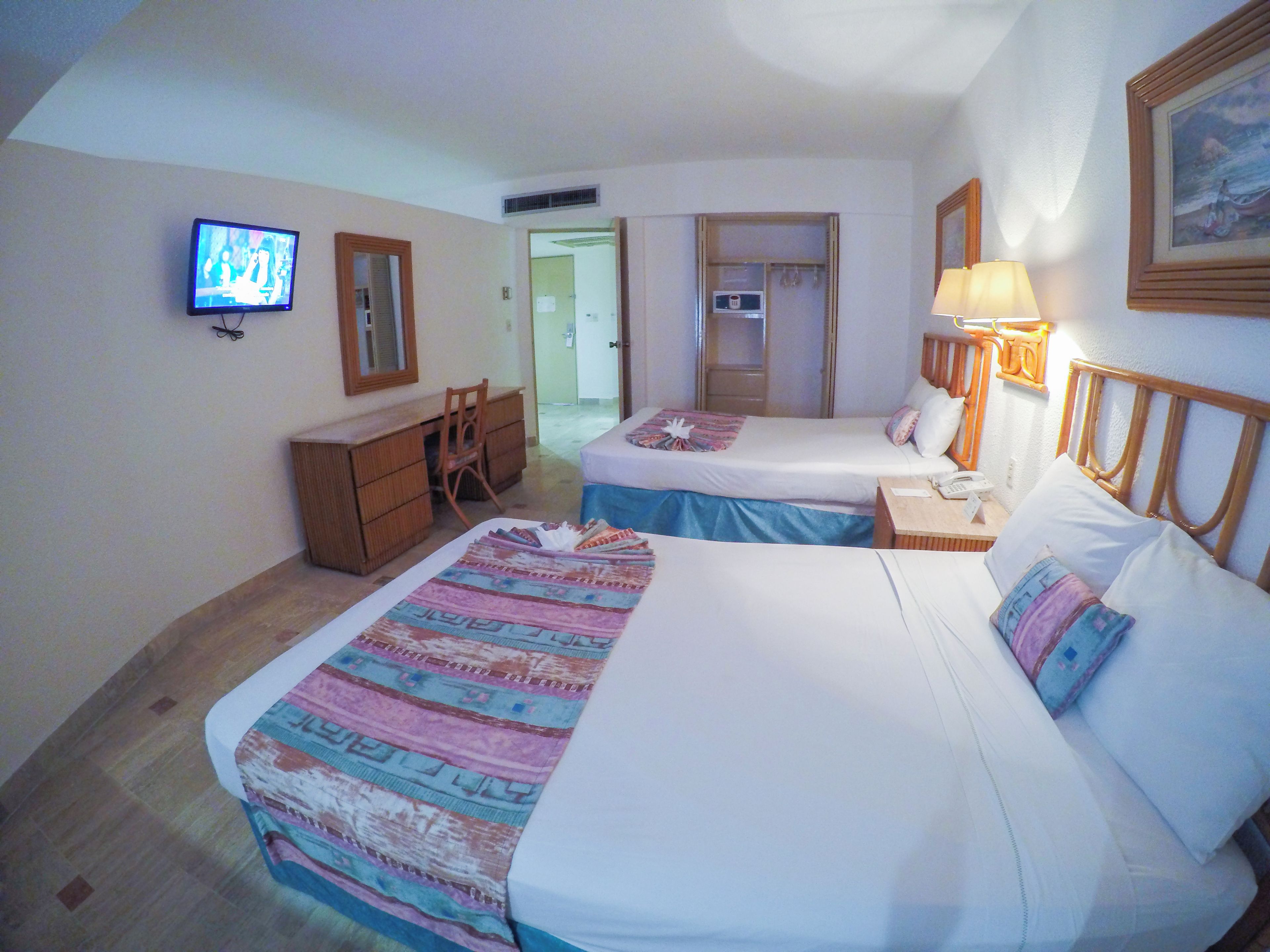 A hotel room with two beds, a desk, a chair, a television, and a lamp.