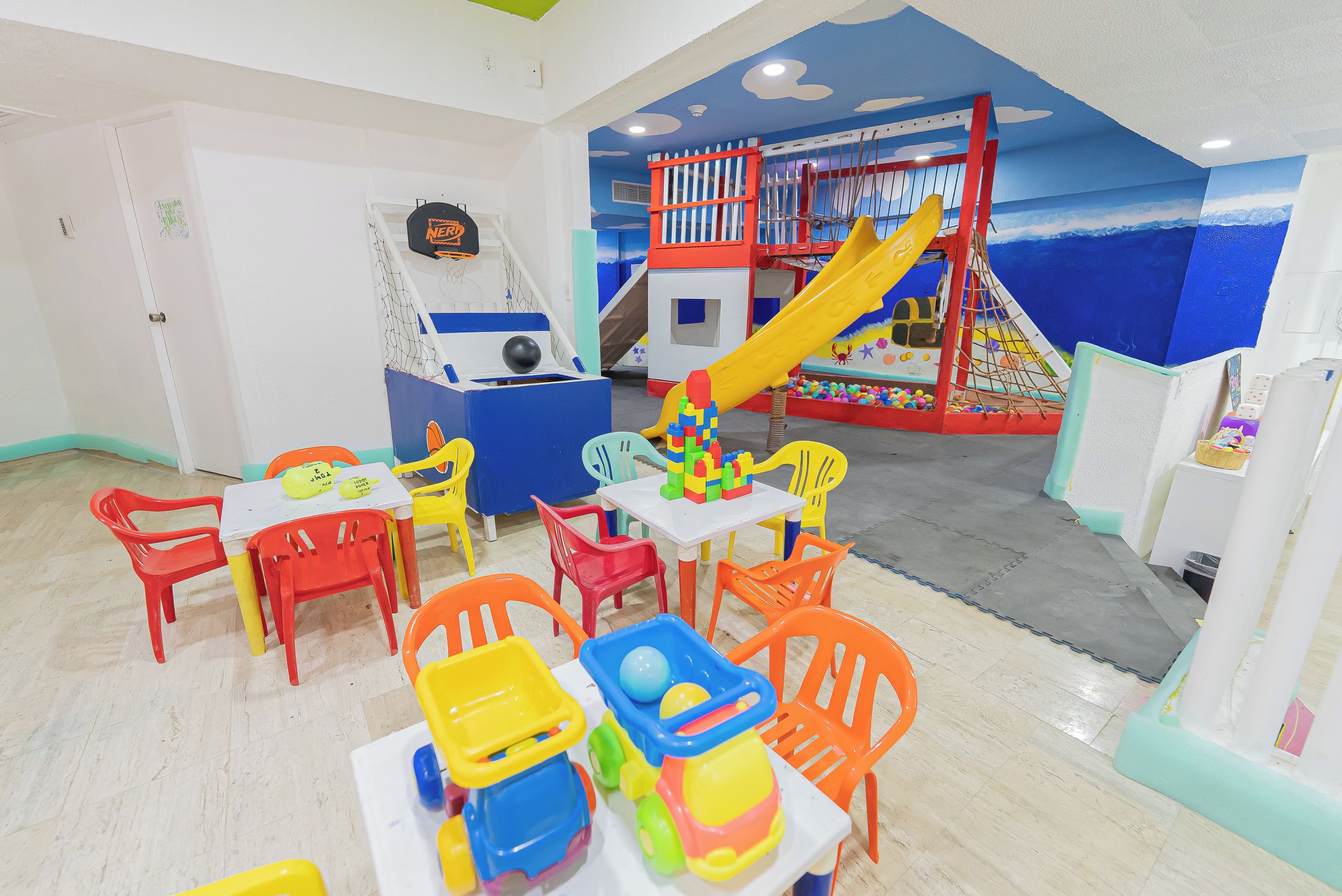 Un espace de jeux pour enfants avec des meubles en plastique de couleurs vives, un toboggan et une structure d’escalade.