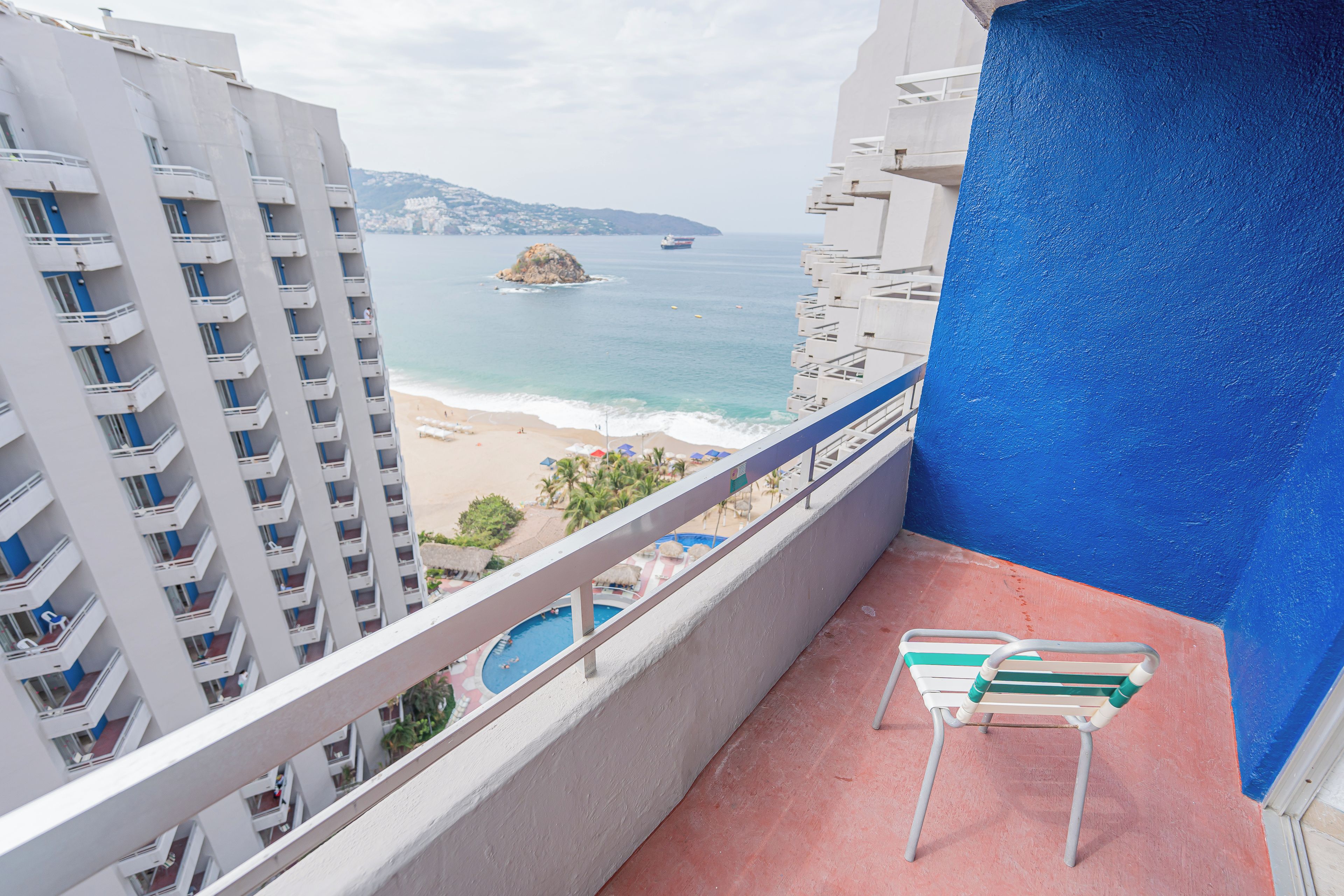 Un balcó amb vista a la platja, una piscina i un edifici amb múltiples balcons.
