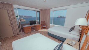 A hotel room with a bed, a desk with a TV, a chair, and a view of the sea. - Playa Suites Acapulco (Acapulco)
