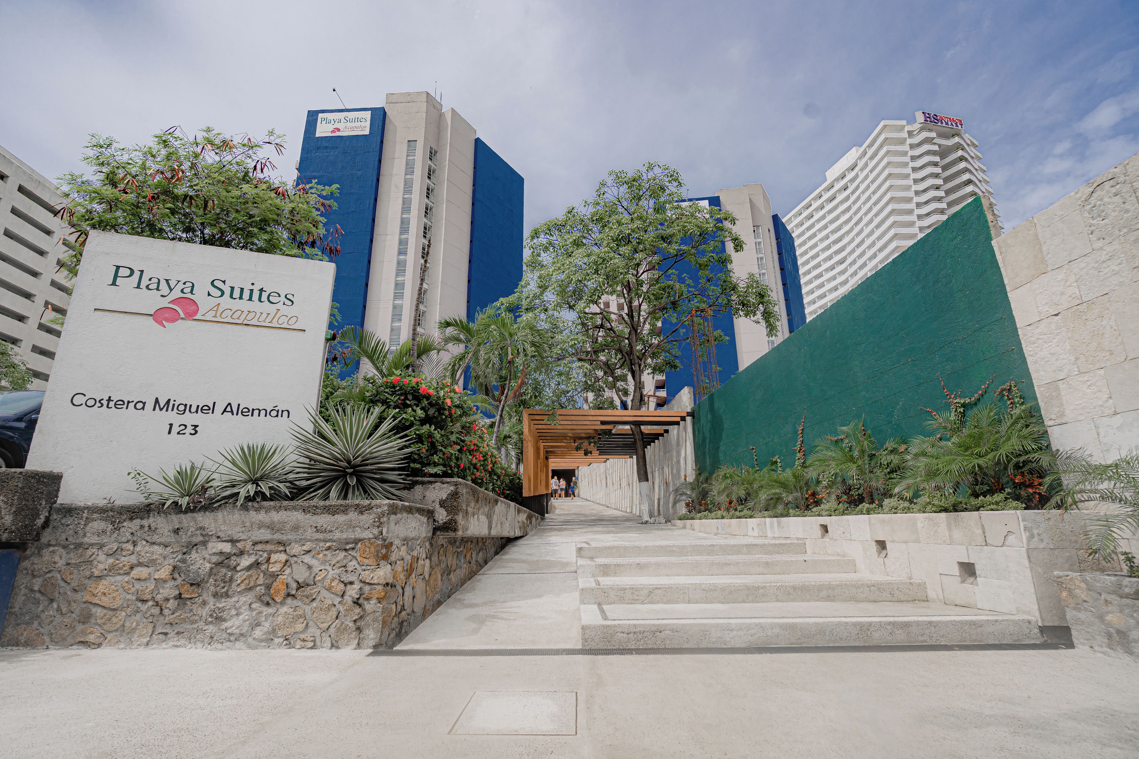 Entrada de un hotel con un letrero que dice 'Playa Suites Acapulco' en 'Coster Miguel Alemán 123'.