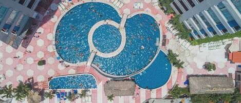 An aerial view of a resort with multiple swimming pools, hexagonal tiles, and palm trees.