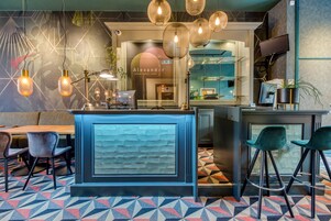 A modern bar area with a blue counter, bar stools, hanging lights, and a patterned floor.