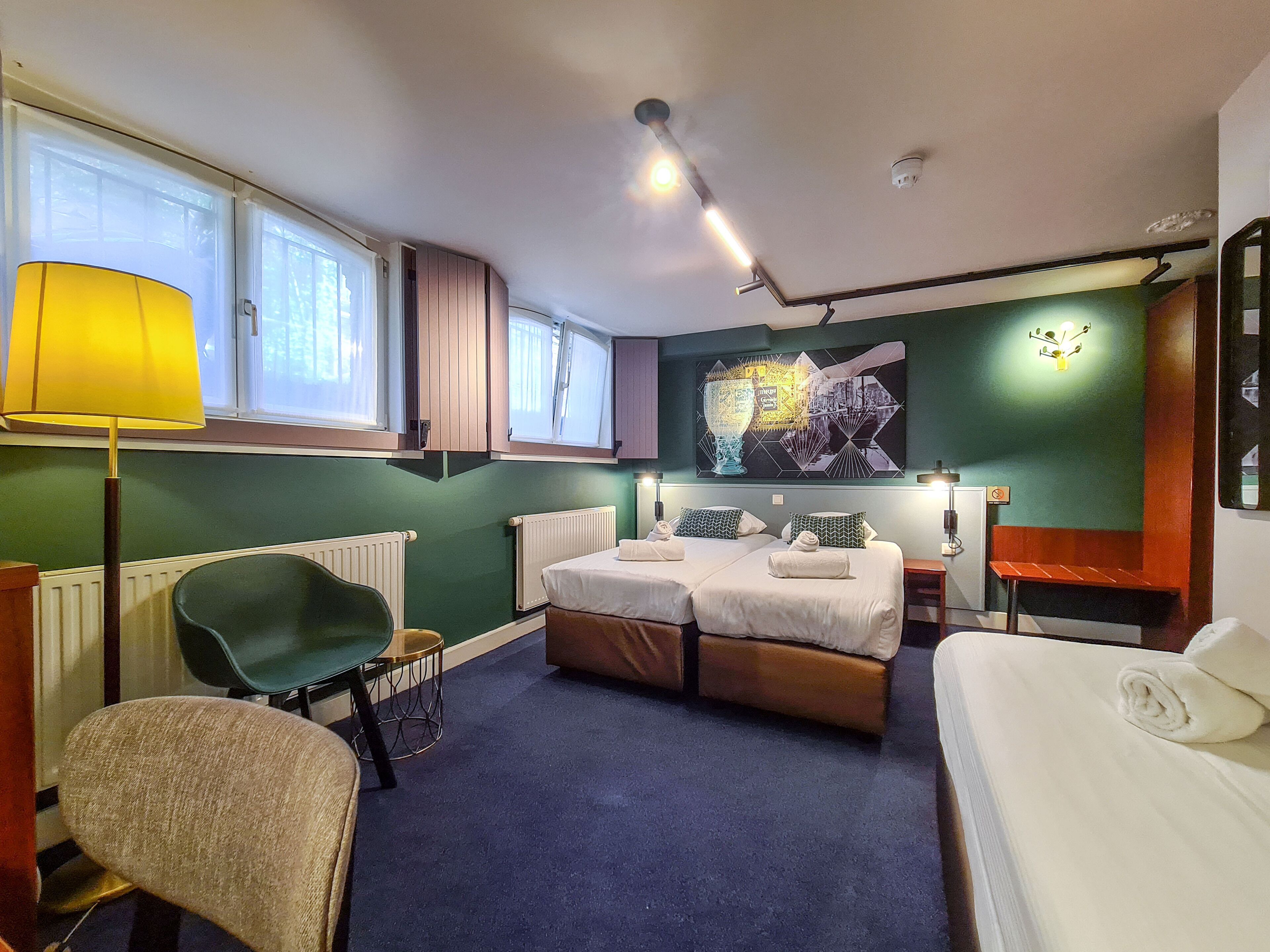 A hotel room with two beds, a desk, a chair, and a radiator.
