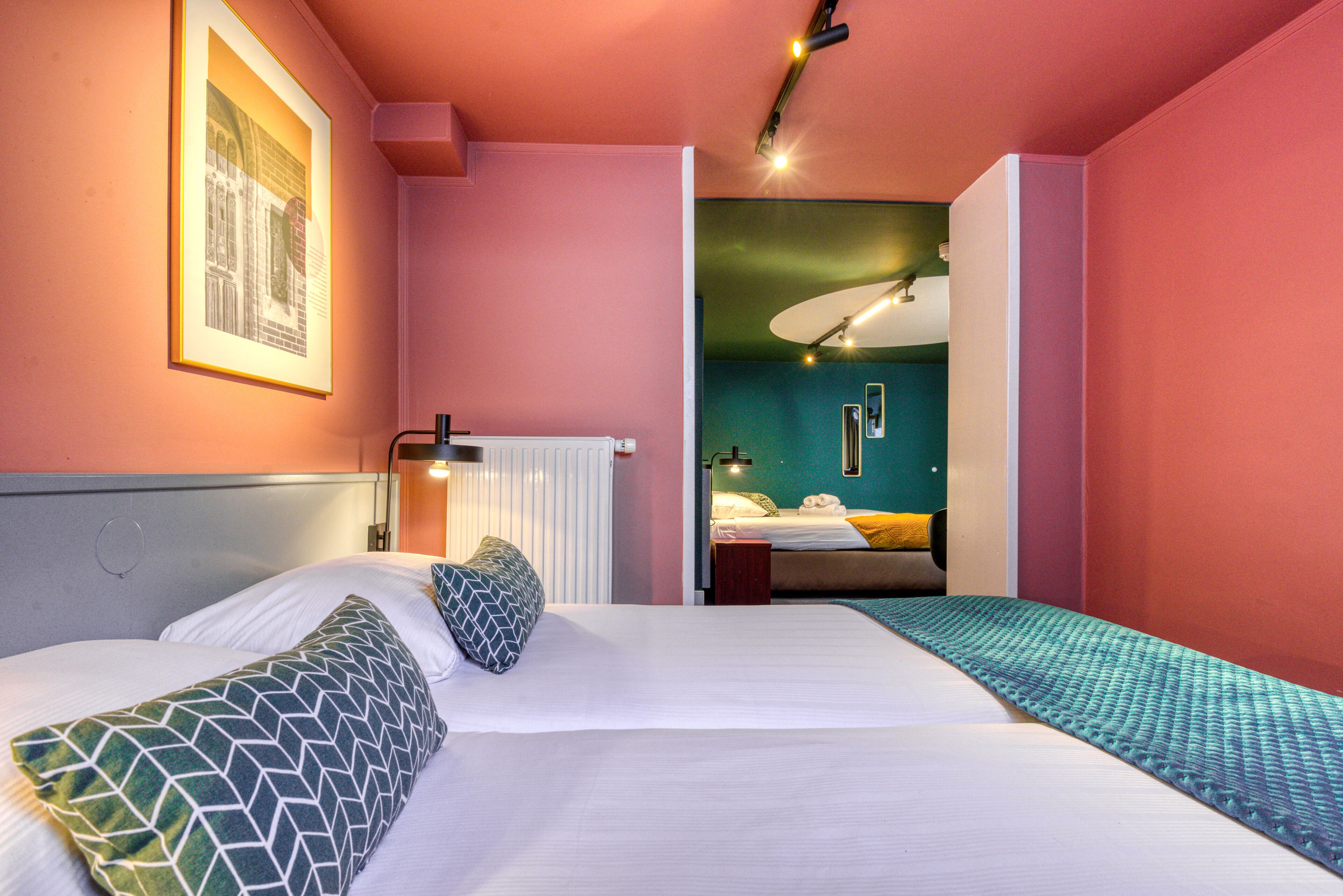 Een hotelkamer met twee bedden, een ingelijste foto aan de muur en uitzicht op een andere kamer.