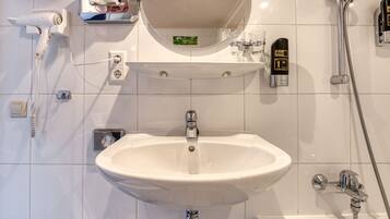 A bathroom with a white sink, a mirror, a hairdryer, a hand wash station, and a shower.