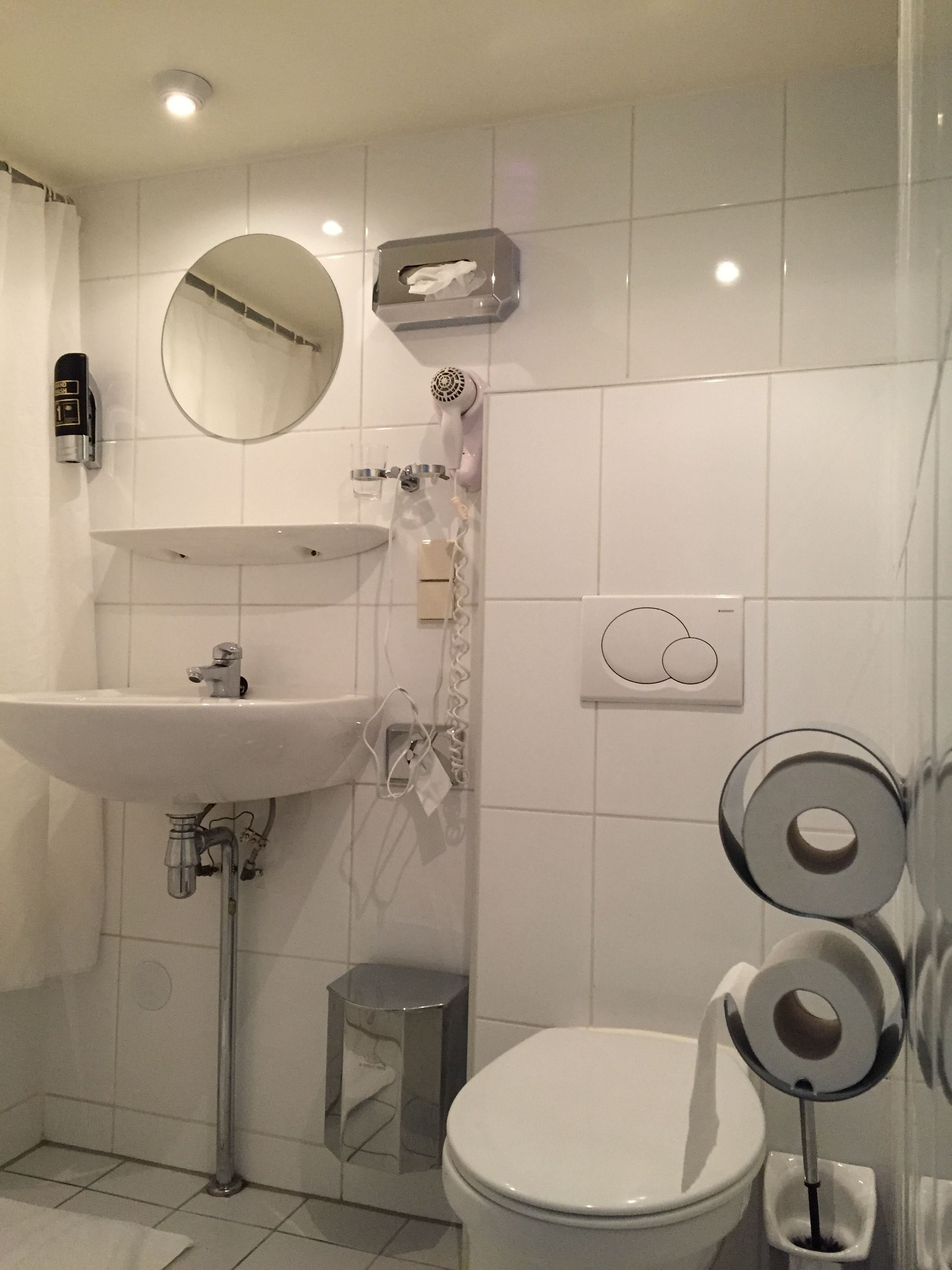 Een badkamer met een wastafel, spiegel, haardroger en toilet.