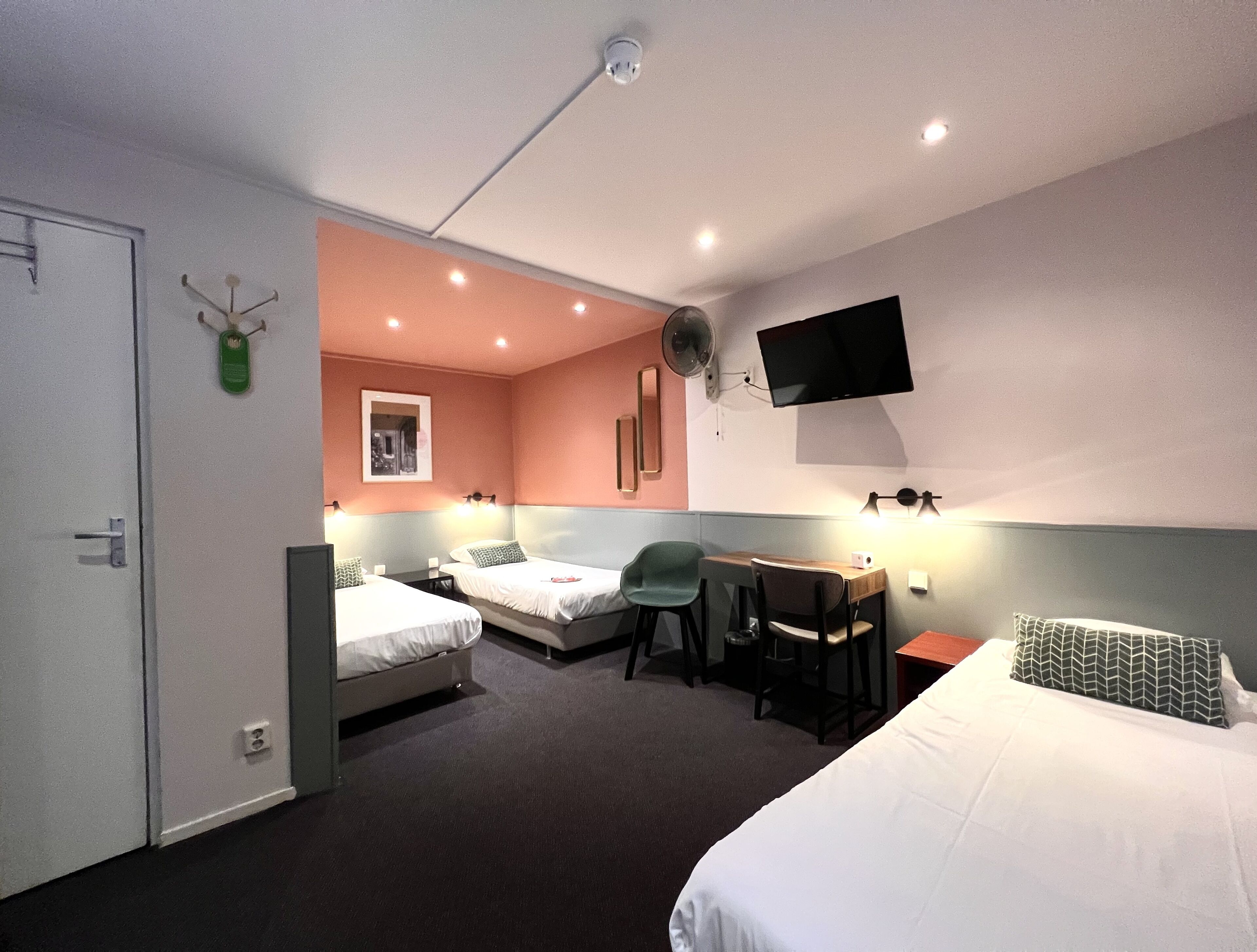 A hotel room with two beds, a desk, a chair, a TV, and a ceiling fan.