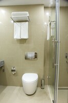 Un baño moderno con inodoro, cabina de ducha con vidrio y un perchero con dos toallas.