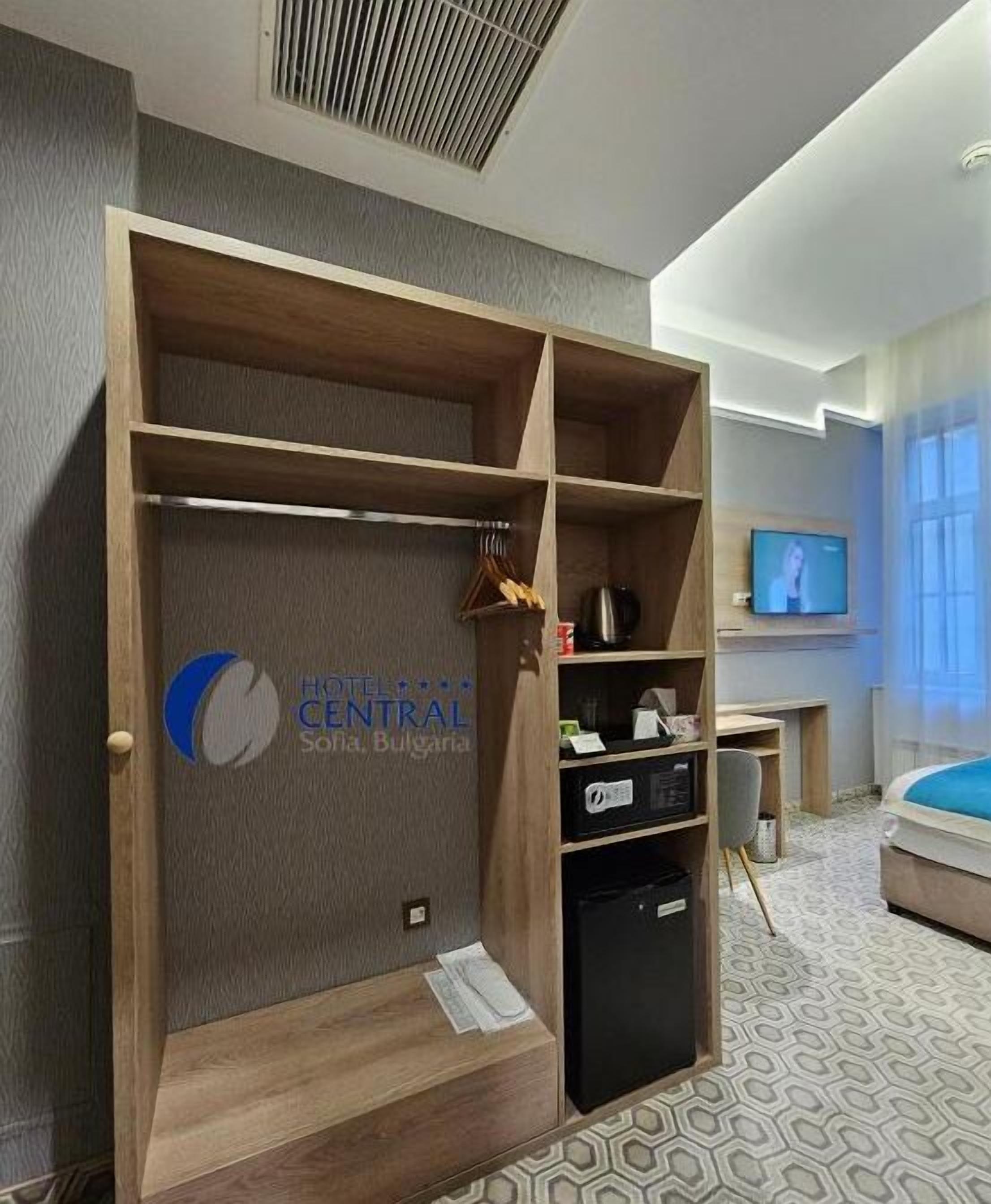 Una habitación de hotel con un armario de madera, televisor, cama y alfombra estampada.