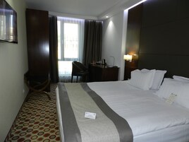 Habitación de hotel con una cama grande, un escritorio, una silla, un televisor y una ventana con cortinas.