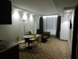 Habitación de hotel con una mesa de comedor, sillas, un sofá, un televisor y una alfombra estampada.