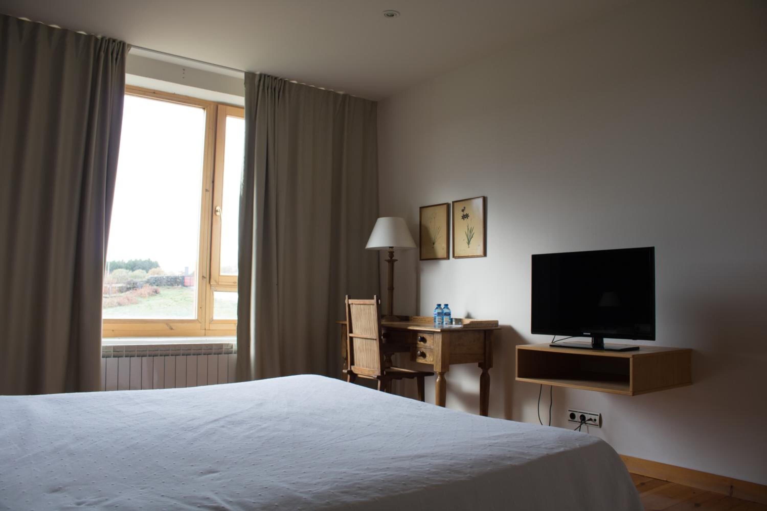 A hotel room with a bed, a desk, a television, and a window with curtains.