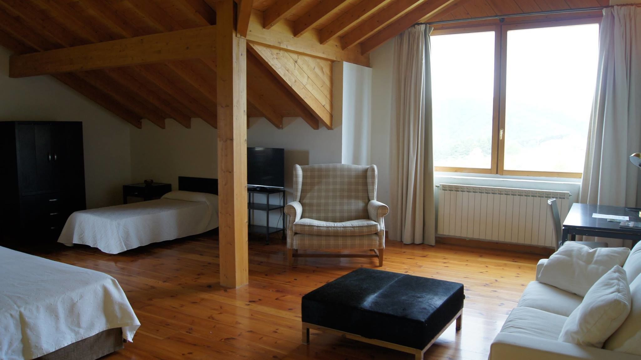 Una habitación con dos camas, una silla, una mesa y un ventanal con cortinas.