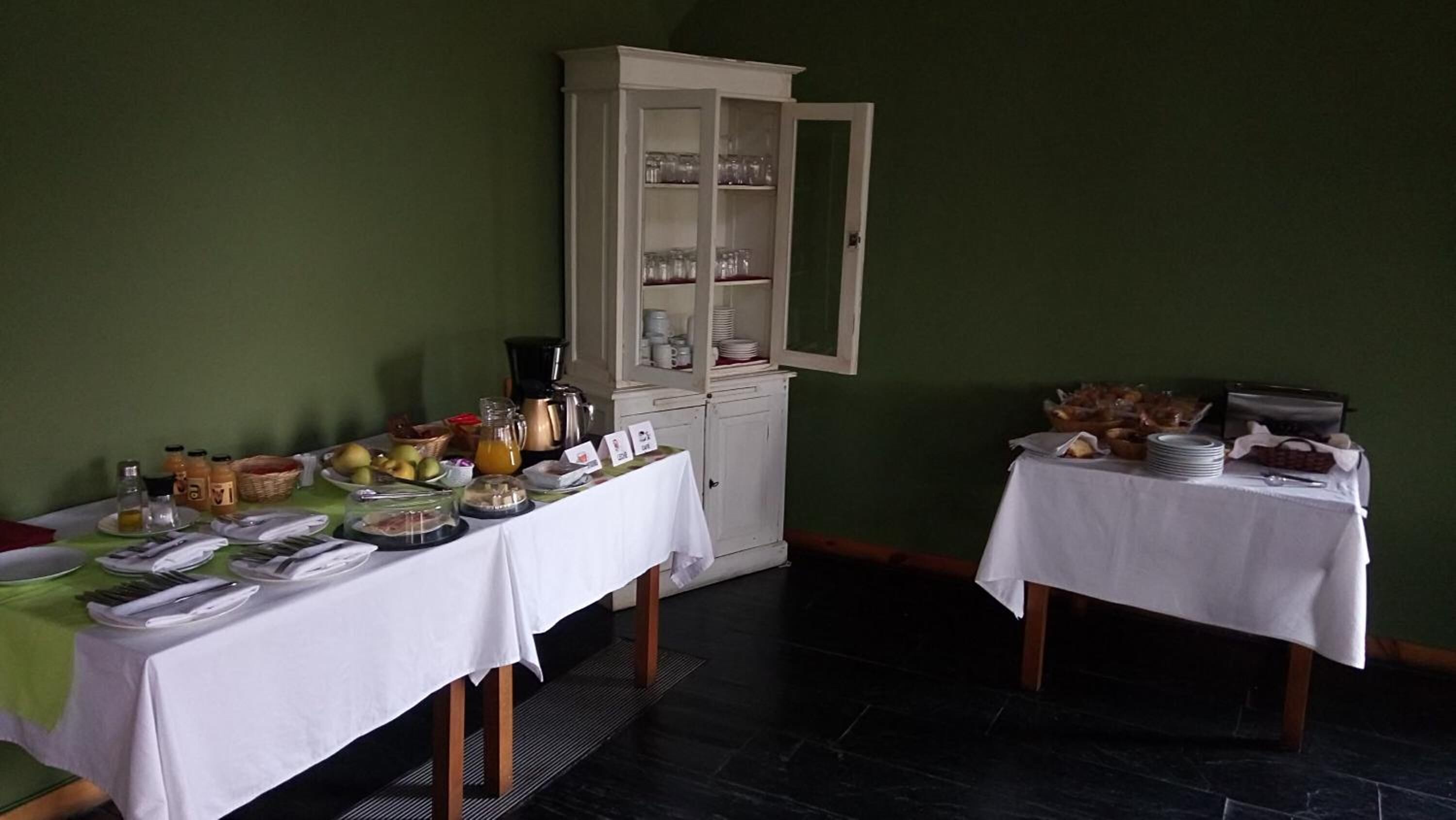 A dining area with two tables set for breakfast, a cabinet with glassware, and a toaster on the right.