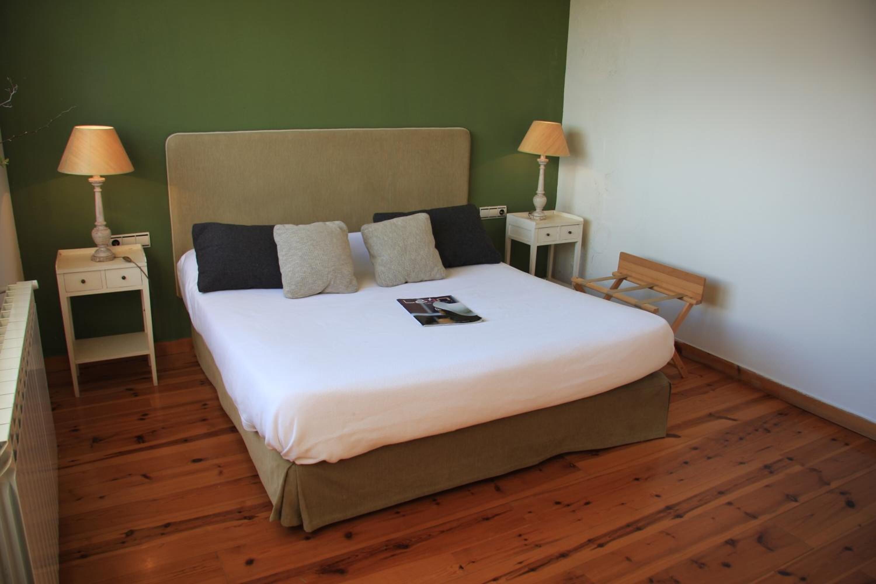 A neatly made bed with a white mattress and a brown headboard in a room with green walls and wooden flooring.