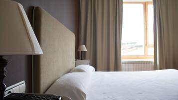 Una habitación de hotel con cama, lámpara, control remoto y ventana con cortinas.