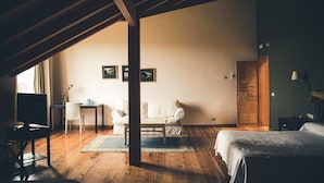 Una habitación amplia con techo alto, vigas de madera, una cama, un escritorio, una silla y un sofá.