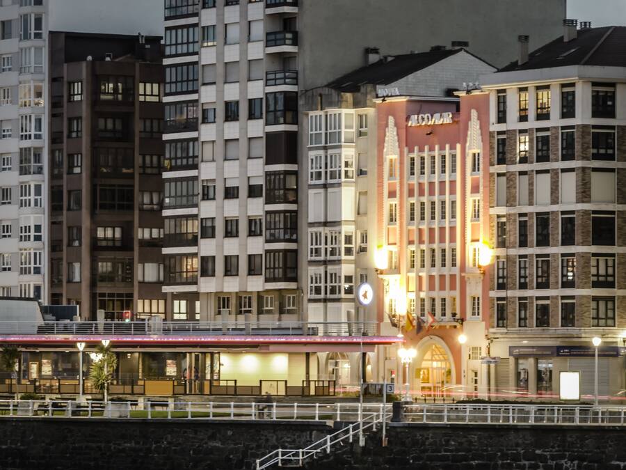 Un hôtel à plusieurs étages, doté d’une façade rouge imposante et d’une enseigne sur laquelle on peut lire « ALCOMAR ».