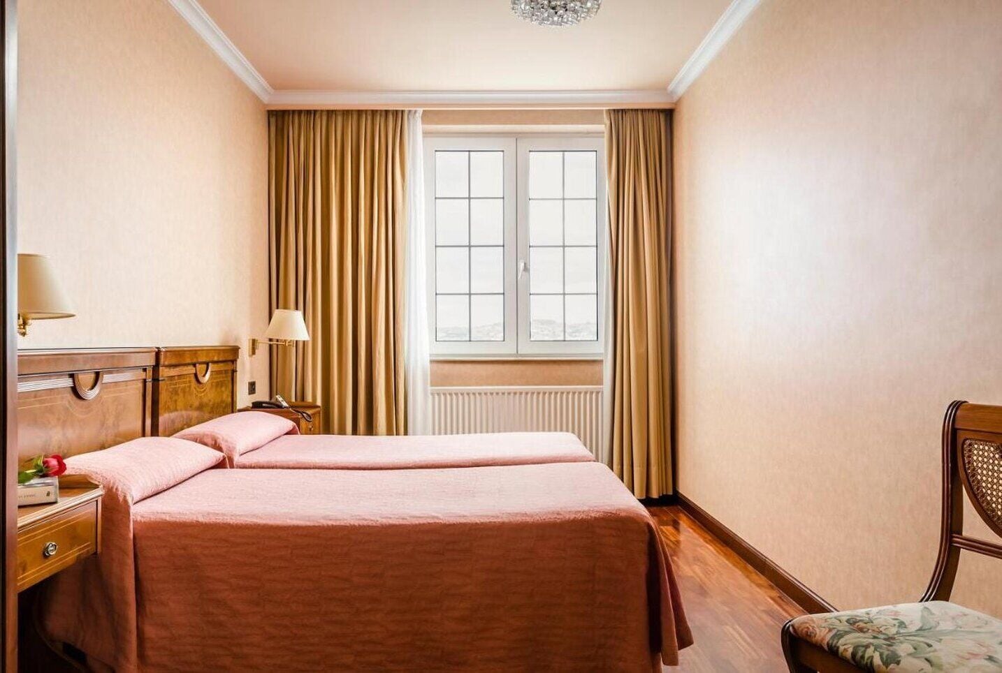Una habitación de hotel con dos camas, un aparador de madera, una silla y una ventana con cortinas.
