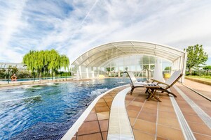 Piscina con dos sillas de descanso y una estructura de vidrio.